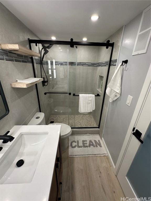 bathroom featuring wood-type flooring, vanity, toilet, and a shower with shower door