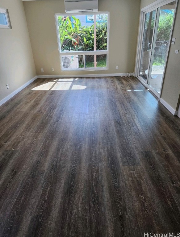 unfurnished room featuring an AC wall unit, a wealth of natural light, and dark hardwood / wood-style flooring