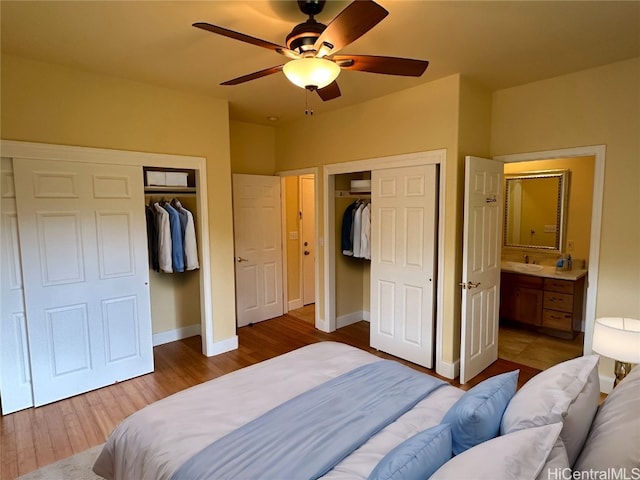 bedroom with two closets, ceiling fan, hardwood / wood-style flooring, ensuite bath, and sink