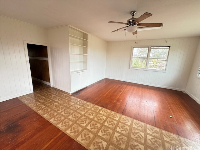 unfurnished room with wood walls, hardwood / wood-style floors, built in features, and ceiling fan