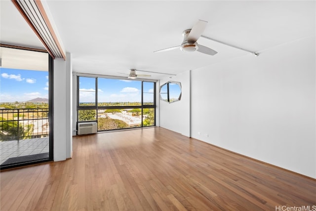 unfurnished room featuring ceiling fan, wood-type flooring, and a wall of windows