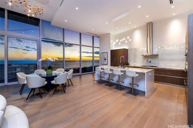 kitchen with backsplash, a kitchen island with sink, pendant lighting, and wall chimney range hood