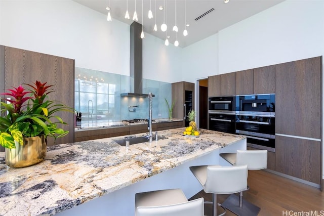 kitchen featuring a kitchen breakfast bar, light stone countertops, wall chimney range hood, and hardwood / wood-style flooring