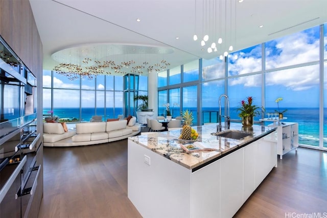 kitchen with a center island with sink, a water view, sink, decorative light fixtures, and white cabinetry