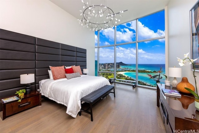 bedroom with expansive windows, hardwood / wood-style floors, a water view, and a notable chandelier