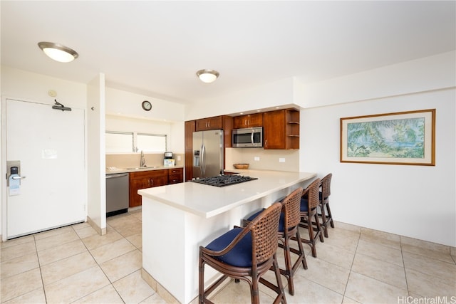 kitchen with kitchen peninsula, stainless steel appliances, light tile patterned floors, and a breakfast bar