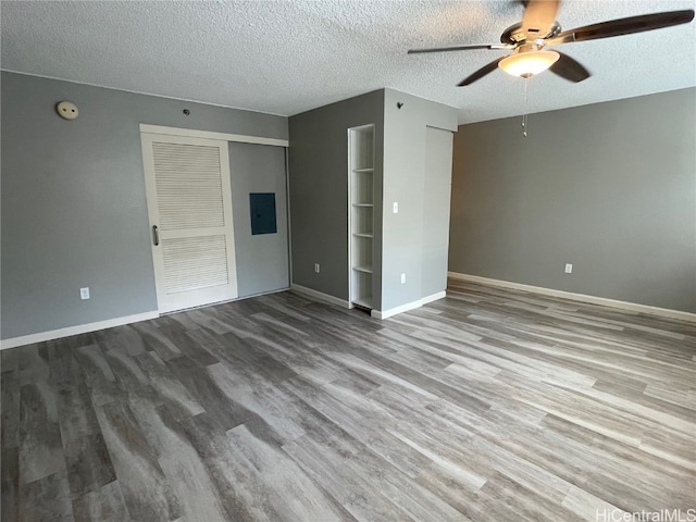 interior space featuring a textured ceiling, electric panel, wood-type flooring, and ceiling fan