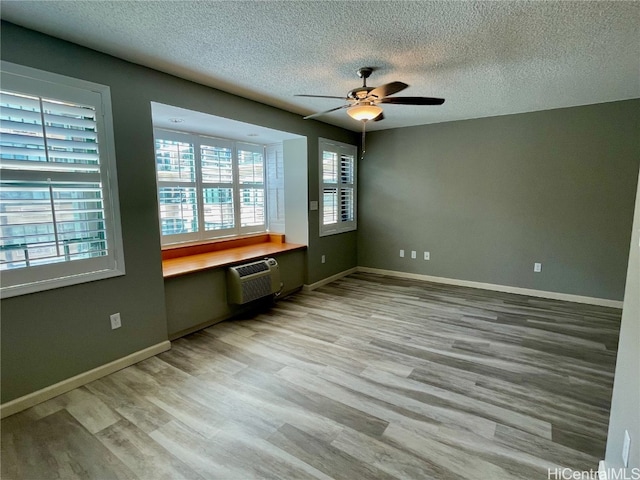 unfurnished bedroom with a wall unit AC, built in desk, hardwood / wood-style floors, a textured ceiling, and ceiling fan