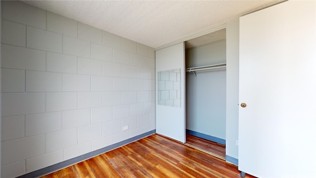 unfurnished bedroom featuring hardwood / wood-style floors, a textured ceiling, and a closet