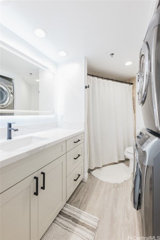 bathroom featuring hardwood / wood-style floors, toilet, vanity, curtained shower, and stacked washer / dryer