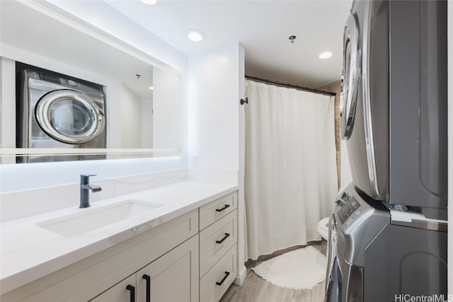 bathroom with toilet, hardwood / wood-style flooring, stacked washer and clothes dryer, and vanity