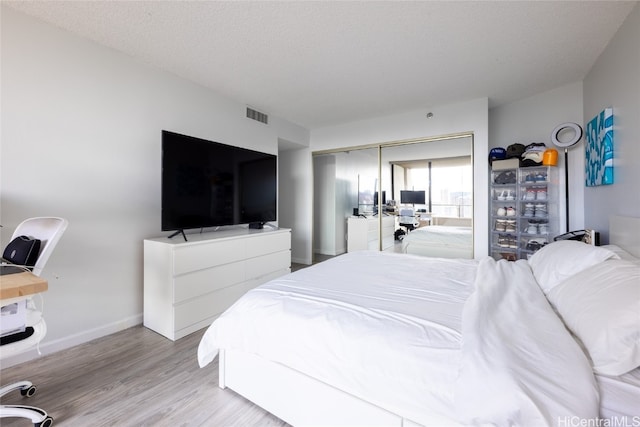 bedroom with a closet, a textured ceiling, and light hardwood / wood-style flooring