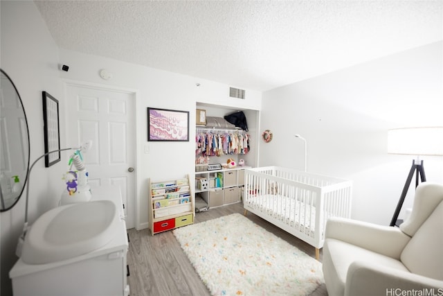 bedroom featuring a textured ceiling, light wood-type flooring, and a crib