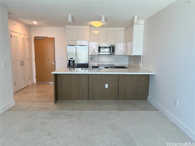 kitchen with sink, light tile patterned floors, appliances with stainless steel finishes, kitchen peninsula, and white cabinets