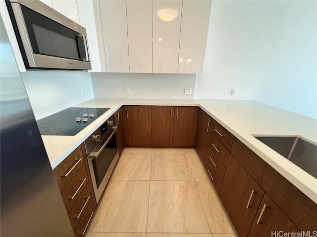 kitchen with sink, appliances with stainless steel finishes, white cabinetry, backsplash, and light stone counters