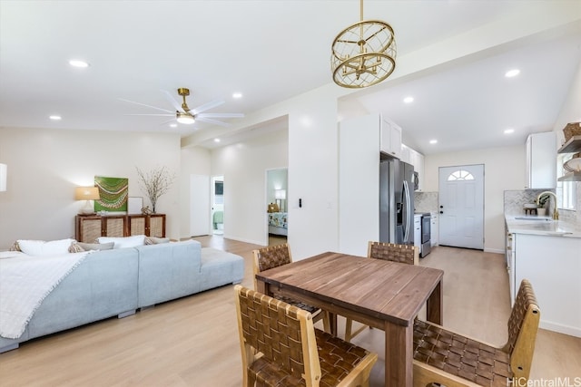 dining space featuring ceiling fan, vaulted ceiling, sink, and light wood-type flooring