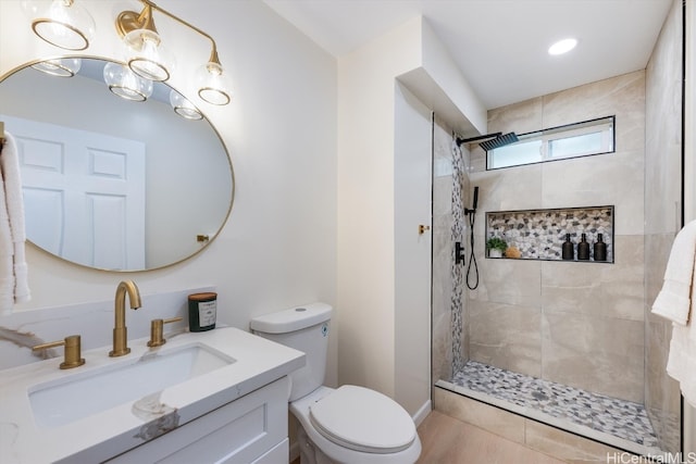 bathroom with a tile shower, toilet, and vanity