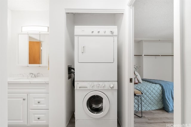 clothes washing area featuring sink, hardwood / wood-style floors, stacked washer and dryer, and a textured ceiling