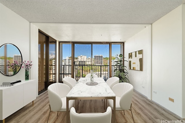 dining area with a textured ceiling, light wood-type flooring, and a wall of windows