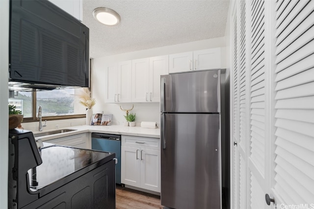 kitchen featuring light hardwood / wood-style floors, appliances with stainless steel finishes, a textured ceiling, and white cabinets