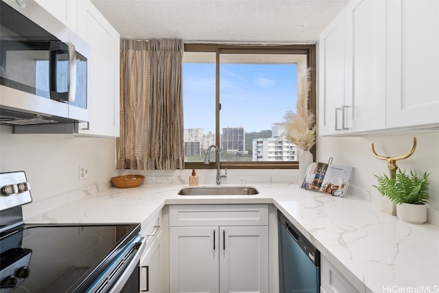 kitchen featuring appliances with stainless steel finishes, white cabinetry, light stone countertops, a textured ceiling, and sink