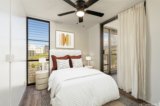 bedroom with ceiling fan, a textured ceiling, access to exterior, floor to ceiling windows, and dark hardwood / wood-style floors