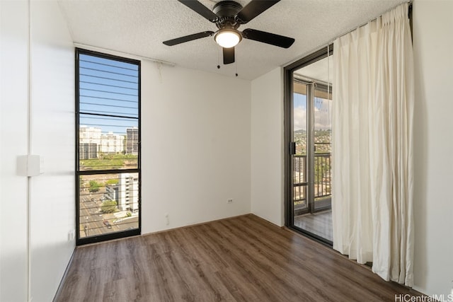 unfurnished room featuring a wall of windows, dark hardwood / wood-style floors, a textured ceiling, and ceiling fan