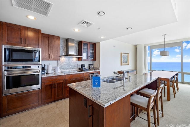 kitchen with oven, a water view, sink, wall chimney exhaust hood, and an island with sink