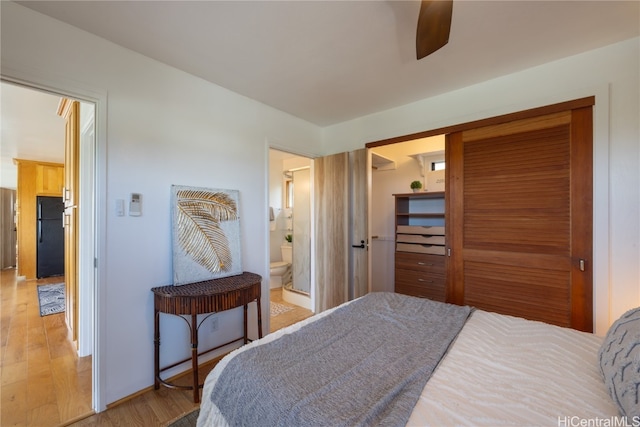 bedroom with ceiling fan, black fridge, ensuite bathroom, light hardwood / wood-style floors, and a closet