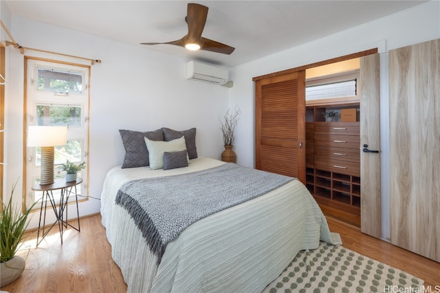 bedroom with ceiling fan, light hardwood / wood-style floors, and a wall mounted air conditioner