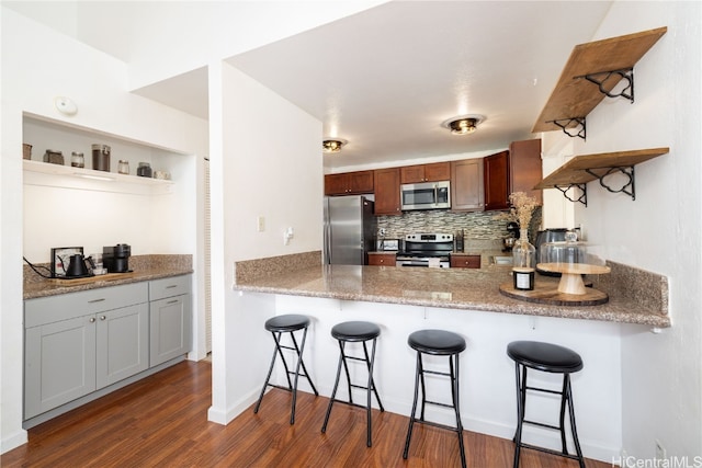 kitchen with kitchen peninsula, decorative backsplash, a breakfast bar, dark hardwood / wood-style floors, and stainless steel appliances