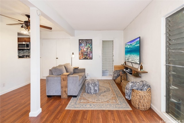 living room with dark wood-type flooring, ceiling fan, and beam ceiling