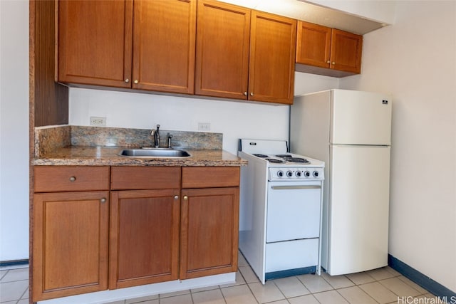 kitchen with white appliances, light tile patterned floors, light stone countertops, a sink, and brown cabinets