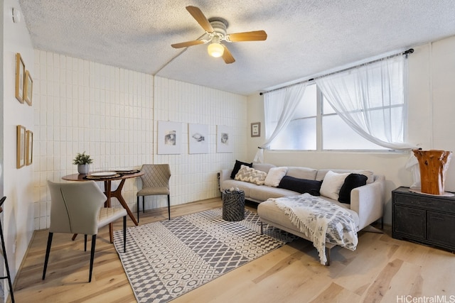 living room featuring ceiling fan, a textured ceiling, light hardwood / wood-style flooring, and tile walls