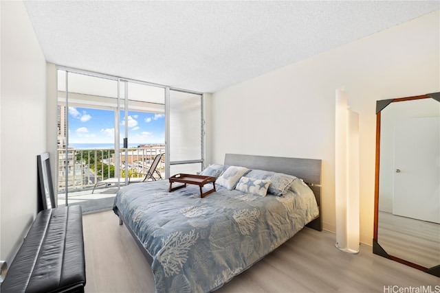 bedroom featuring access to outside, a textured ceiling, expansive windows, and light hardwood / wood-style flooring