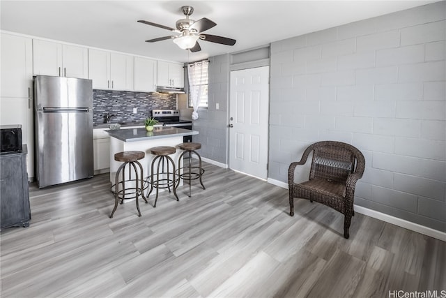 kitchen featuring stainless steel appliances, white cabinetry, a kitchen breakfast bar, a kitchen island, and light wood-type flooring