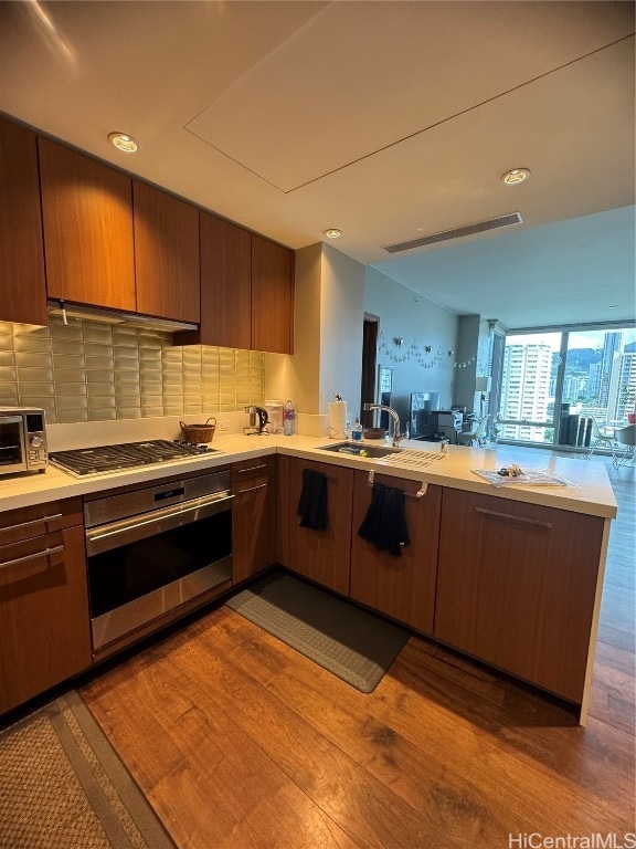 kitchen with decorative backsplash, kitchen peninsula, stainless steel appliances, and hardwood / wood-style flooring