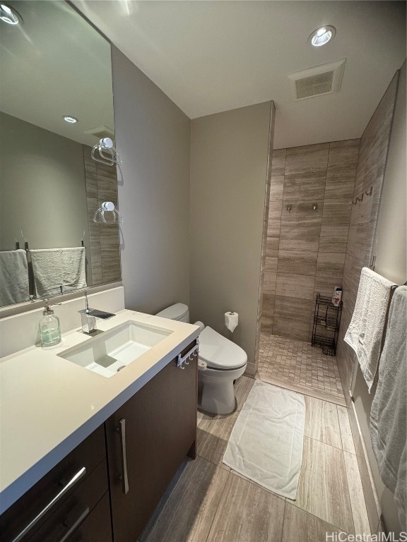 bathroom featuring toilet, hardwood / wood-style floors, vanity, and tiled shower