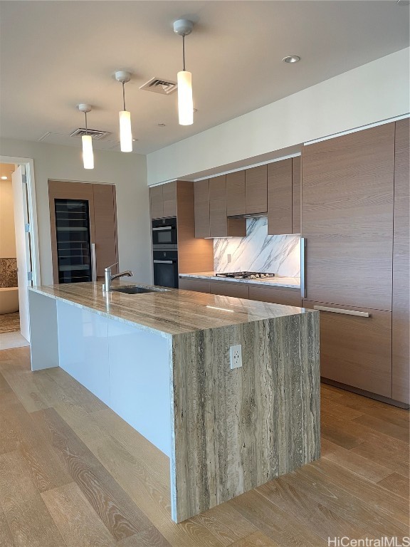 kitchen featuring double oven, light hardwood / wood-style flooring, sink, decorative light fixtures, and light stone counters