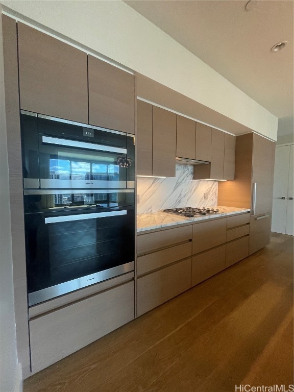 kitchen featuring stainless steel gas stovetop, double oven, light wood-type flooring, and backsplash