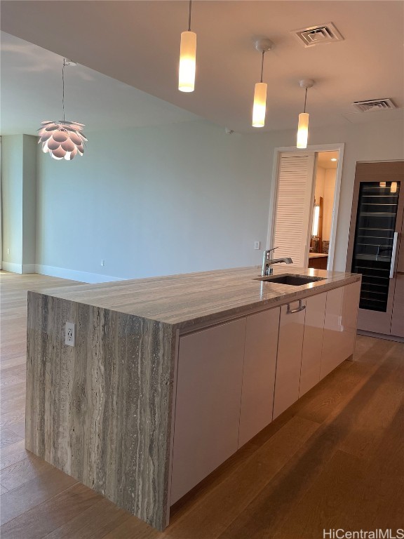 kitchen featuring hardwood / wood-style floors, sink, white cabinets, and pendant lighting