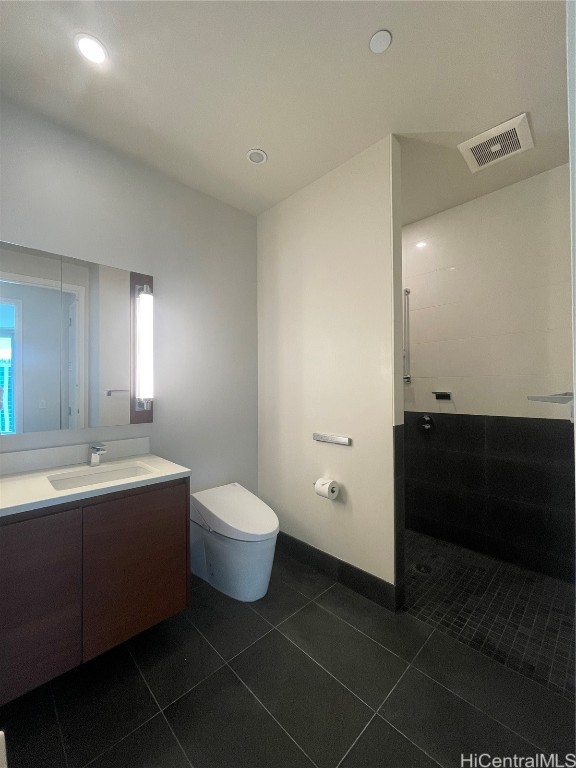 bathroom with toilet, vanity, a tile shower, and tile patterned floors