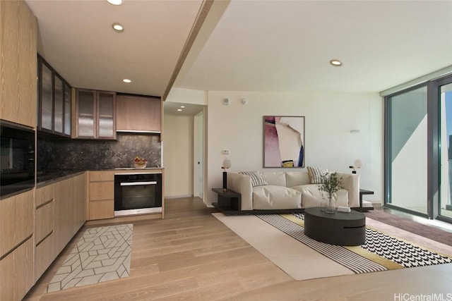 kitchen featuring light brown cabinets, backsplash, oven, light wood-type flooring, and a wall of windows