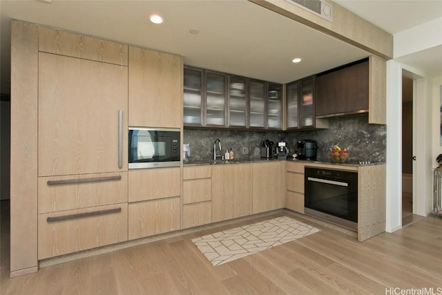 kitchen with tasteful backsplash, light brown cabinets, light hardwood / wood-style flooring, and appliances with stainless steel finishes