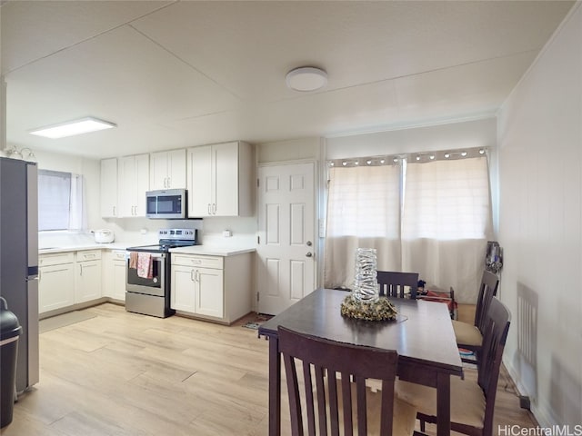 kitchen with appliances with stainless steel finishes, white cabinets, and light hardwood / wood-style floors