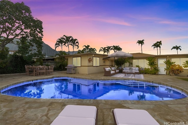 pool at dusk featuring an outdoor living space, a patio area, and grilling area