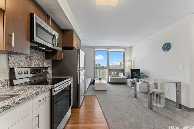 kitchen with light stone countertops, light carpet, decorative backsplash, white cabinets, and appliances with stainless steel finishes