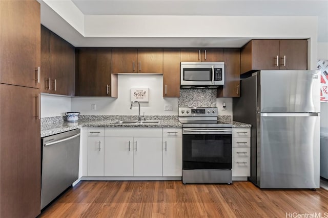 kitchen with hardwood / wood-style floors, white cabinets, sink, appliances with stainless steel finishes, and light stone counters