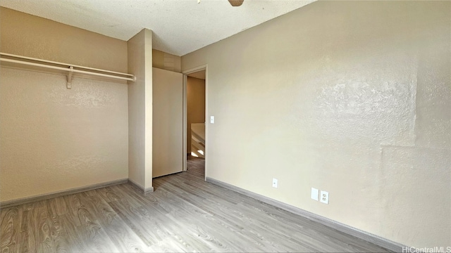 unfurnished bedroom featuring ceiling fan, a closet, a textured ceiling, and light wood-type flooring