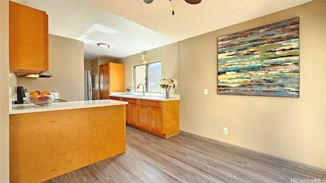 kitchen featuring ceiling fan, sink, kitchen peninsula, light wood-type flooring, and range